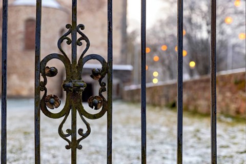 Decorated iron fence in the foreground with a brick building and illuminated lights in the