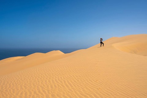 Photographer taking pictures with camera, standing on a dune, sand dunes with wave patterns, sea of