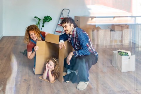 Happy family exploring their new house, parents and young daughter having fun playing with