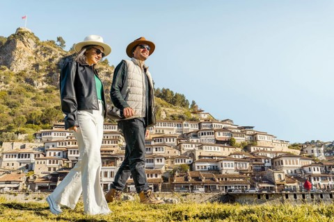 Happy travel couple walking historic Berat hillside town Albania traditional Ottoman houses sunny