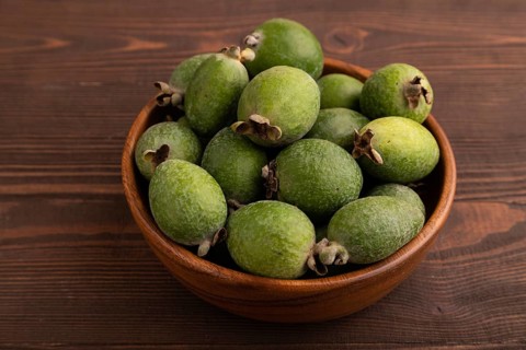 Ripe Feijoa in wooden bowl on brown wooden background, side view, close up, minimalism