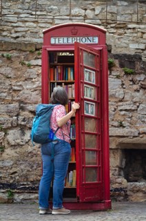 Elderly woman looks at old red English telephone box, telephone, serves as library, public