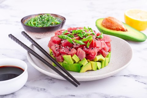 Fresh tuna tartare with avocado served on a marble table with soy sauce and seaweed salad