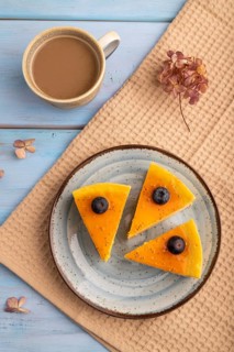 Cheesecake with mango cream, cup of coffee, on blue wooden background with beige textile, close up,