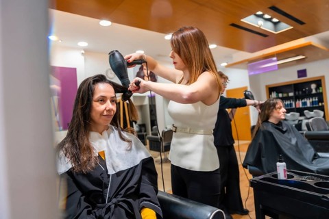 Hairdresser blow drying a woman's hair with a round brush in a well lit salon, providing hair care