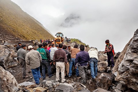 People work together to move a rock on a foggy mountain road with a tractor, rockslide on the pass