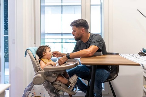 Father feeding his baby son pureed food in a high chair at home, nurturing bonding and healthy