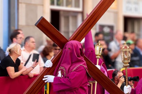 Participants in purple robes carry a large cross in front of spectators, Good Friday procession,