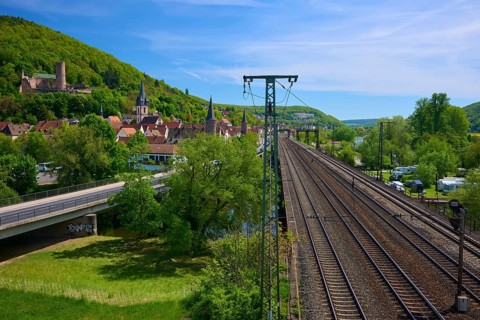 A town with railway lines and power poles, surrounded by green nature and hills, Gemünden am Main,