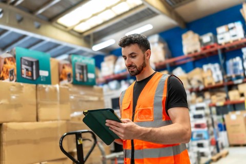 Male employee wearing a safety vest checking stock and scanning products on a digital tablet in a