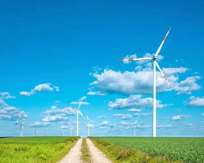 Dirt road leads through green fields with wind turbines, blue sky with cumulus clouds,