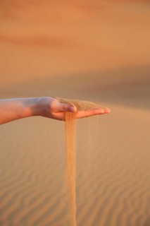 Hand holding trickling sand in a quiet desert landscape at sunset, A woman's hand lets red desert