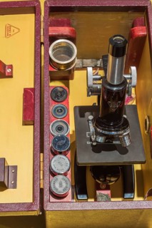 Stored vintage black Bausch & Lomb research microscope with objective lenses in opened brownish red