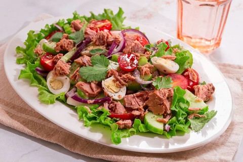 A fresh salad is served on a white platter. The salad includes tuna, cherry tomatoes, cucumber,