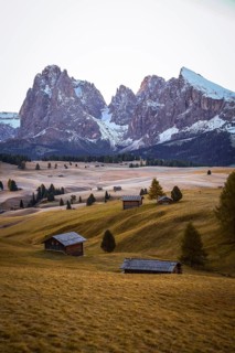 Snow-covered mountains and quiet meadows with scattered wooden huts, view over the autumnal Seiser