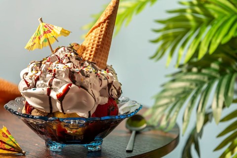 A decorated ice cream sundae with cream, umbrella and waffle on a table