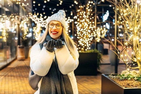 Young woman in winter attire enjoying festive lights outdoors. A woman wearing a white winter coat,