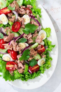 A fresh salad is served on a white platter. The salad includes tuna, cherry tomatoes, cucumber,