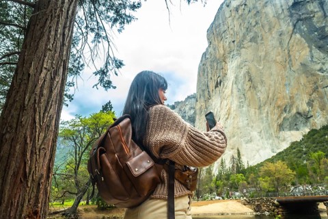 Woman traveler wearing a backpack and knitted sweater standing by the merced river, photographing