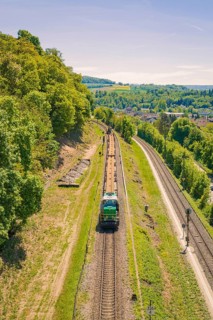 A train travels through a green, hilly landscape in clear summer weather, electrification of the