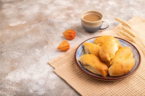Homemade pies with jam and curd, cup of coffee, on brown concrete background with beige textile,