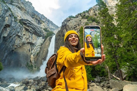 Young woman in yellow raincoat holding a smart phone, recording a selfie video while visiting lower