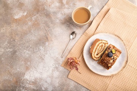 Sweet loaf with cream and caramel, cup of coffee, on brown concrete background with linen beige