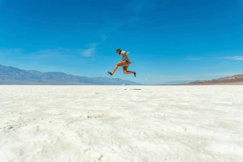 Man jumping joyfully in a vast salt flat landscape under a clear blue sky, experiencing freedom and