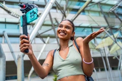 Young content creator recording herself with a smartphone on a gimbal, smiling and gesturing while