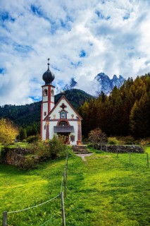 Picturesque church against an autumn mountain backdrop, surrounded by forests and green meadows