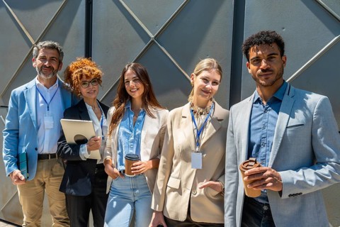 Group of five adult professionals standing outdoors, smiling towards the camera, representing