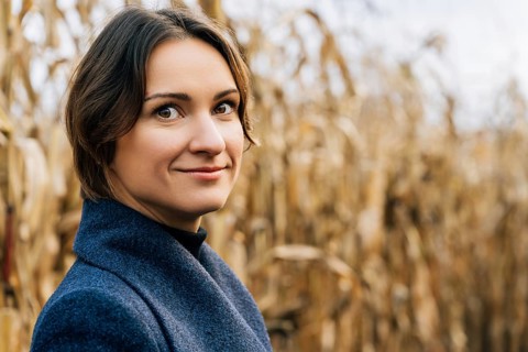Young woman with short brown hair smiling while standing in autumn in agricultural field