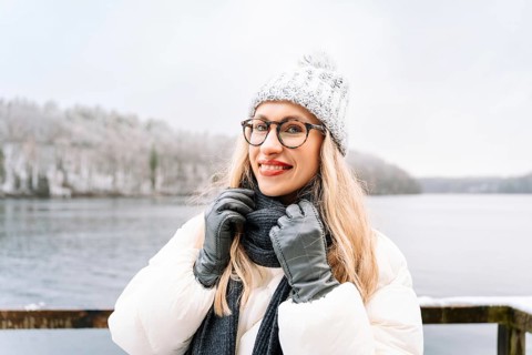 Smiling woman outdoors on a cold winter day near a snowy forest and lake. A woman wearing a white