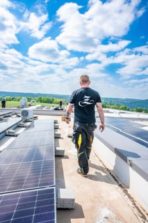 Man walking along solar panels on a roof, blue sky, green nature, PV installation, Perrot company,