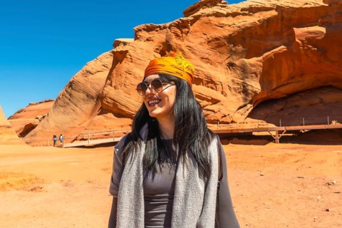 Young woman smiling and wearing sunglasses with an orange bandana on her head, enjoying a desert