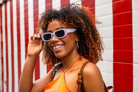 Young black woman with curly hair and stylish sunglasses smiling, portraying joy and modern urban