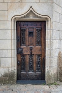 Close-up of a closed, antique entrance door made of dark natural wood with ornate decorations in