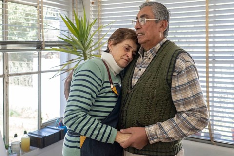 Mature woman rests her head against her partner's chest in a quiet, tender embrace inside their