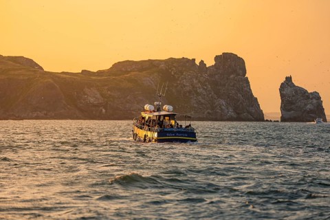A boat at dusk near rock formations surrounded by calm water, Howth, Ireland