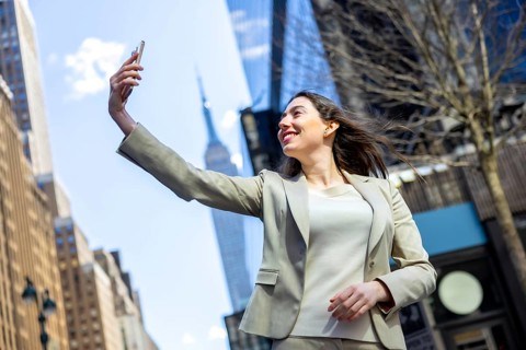Young smiling businesswoman capturing a selfie with her smartphone against the urban backdrop of