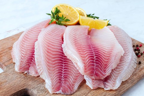Fresh Tilapia fillet, on a wooden chopping board, with lemon and herbs, ready to cook in the
