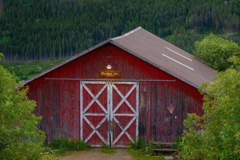 View of an illuminated entrance to an old barn in the mountains at dusk, Gol, Halligdal, Buskerud,