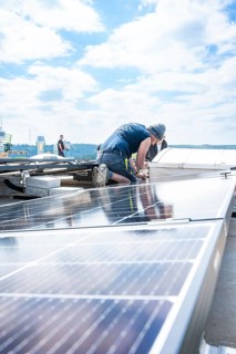 Craftsman working on a roof with solar panels under a blue sky, PV Montage, Perrot company, Calw,