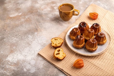 Golden caramelized Canele cookies dessert, cup of coffee, on brown concrete background with beige