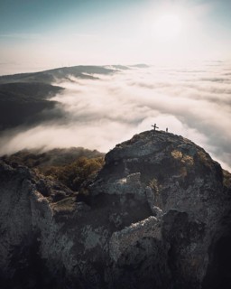 Dramatic Aerial view of Kojori fortressabove the clouds with person sillhouette and cross on top.