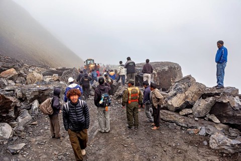 People wearing protective vests watch a foggy construction site, rockslide on the pass road towards