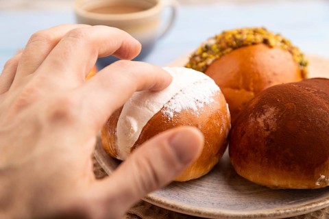 Maritozzo traditional Italian bun dessert with hand, cup of coffee, on blue wooden background with