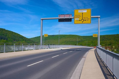 Empty road on a bridge with road signs and views of green hills and blue sky, Mainbrücke, Gemünden