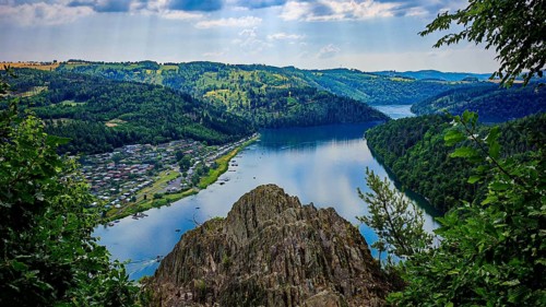 A wide view from Bockfelsen of a quiet lake and a camping site, framed by thick forests and rocks,