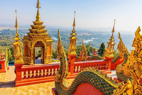 Gilded dragon figures, a gilded pagoda in the back, at the Buddhist temple Wat Phra That Don Phra